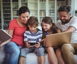 Happy family sitting on sofa and using laptop, mobile phone and digita